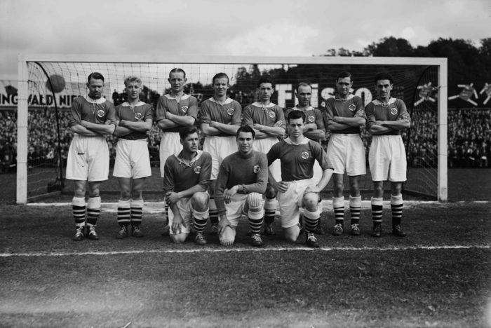 Det norske herelandslaget i fotball. lagbilde. Tre sitter på huk foran, resten står bak foran mål.