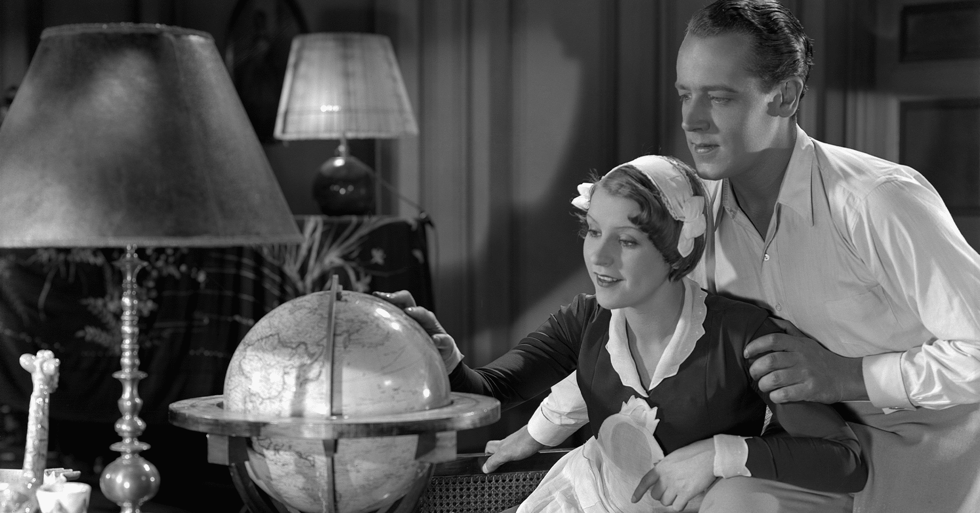 Stillbilde fra en film. En kvinne og mann ser og tar på en globus