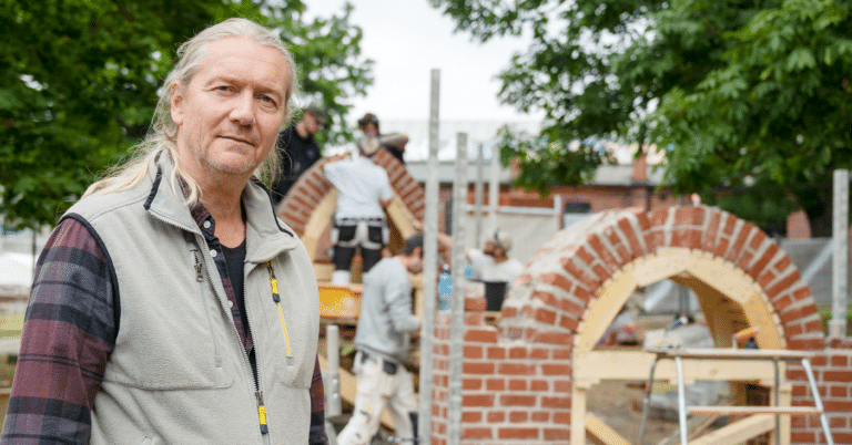 En mann med arbeidsklær står foran en struktur med murstein