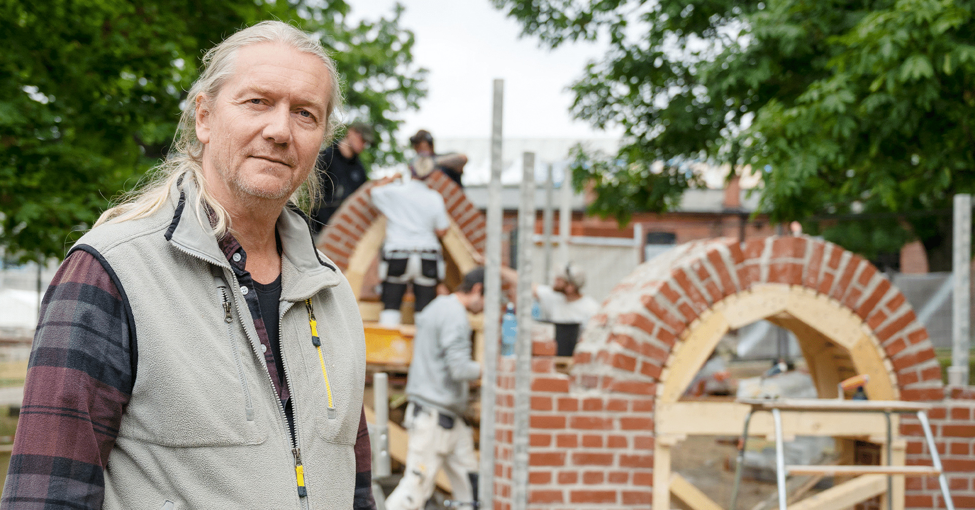 En mann med arbeidsklær står foran en struktur med murstein