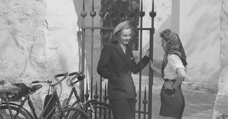 Et bilde i svart-hvitt som viser to kvinner som snakker flørtende med hverandre