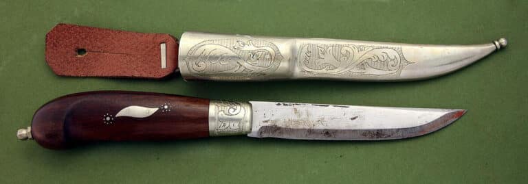 Bildet viser en kniv og en slire i typisk hedenberg-stil. Sliren har et pent mønster, mens kniven har mønster langs skaftet, som er av en mørkebrun tresort.