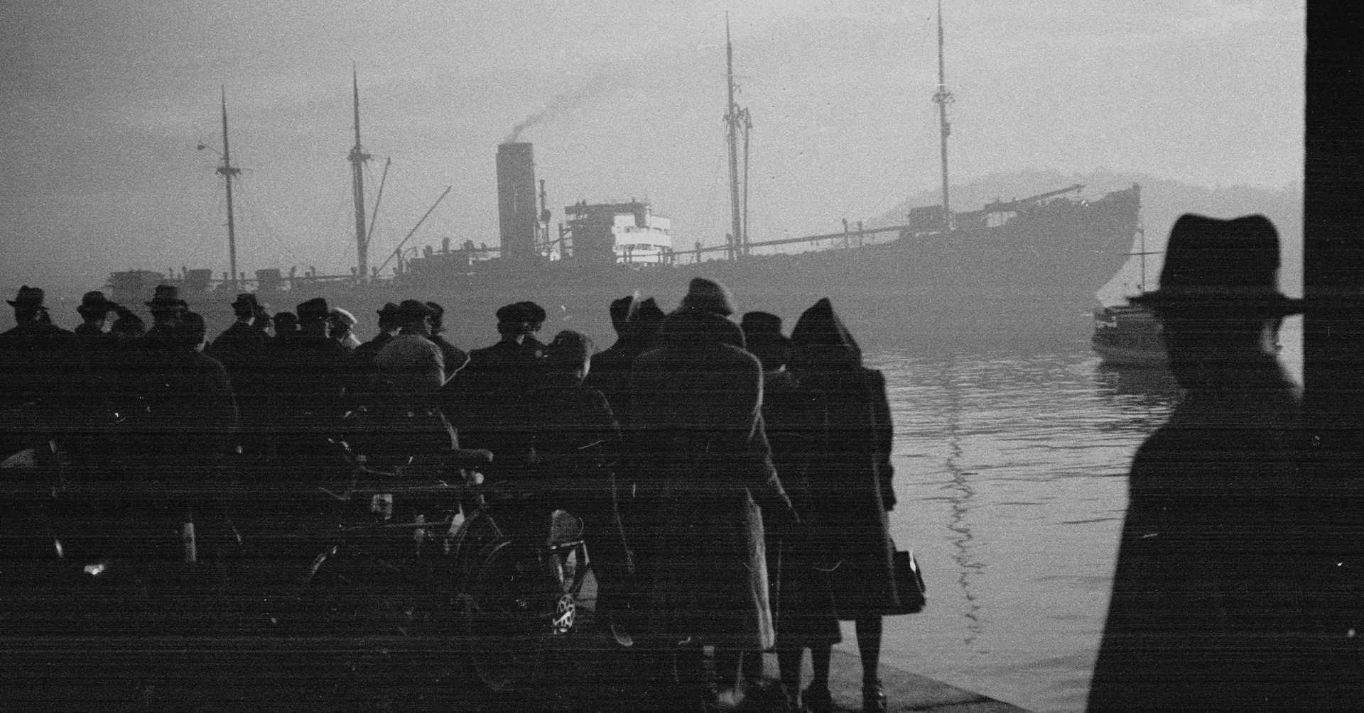 Svart hvitt bilde viser en gruppe mennesker som ser utover Oslofjorden og et stort skip