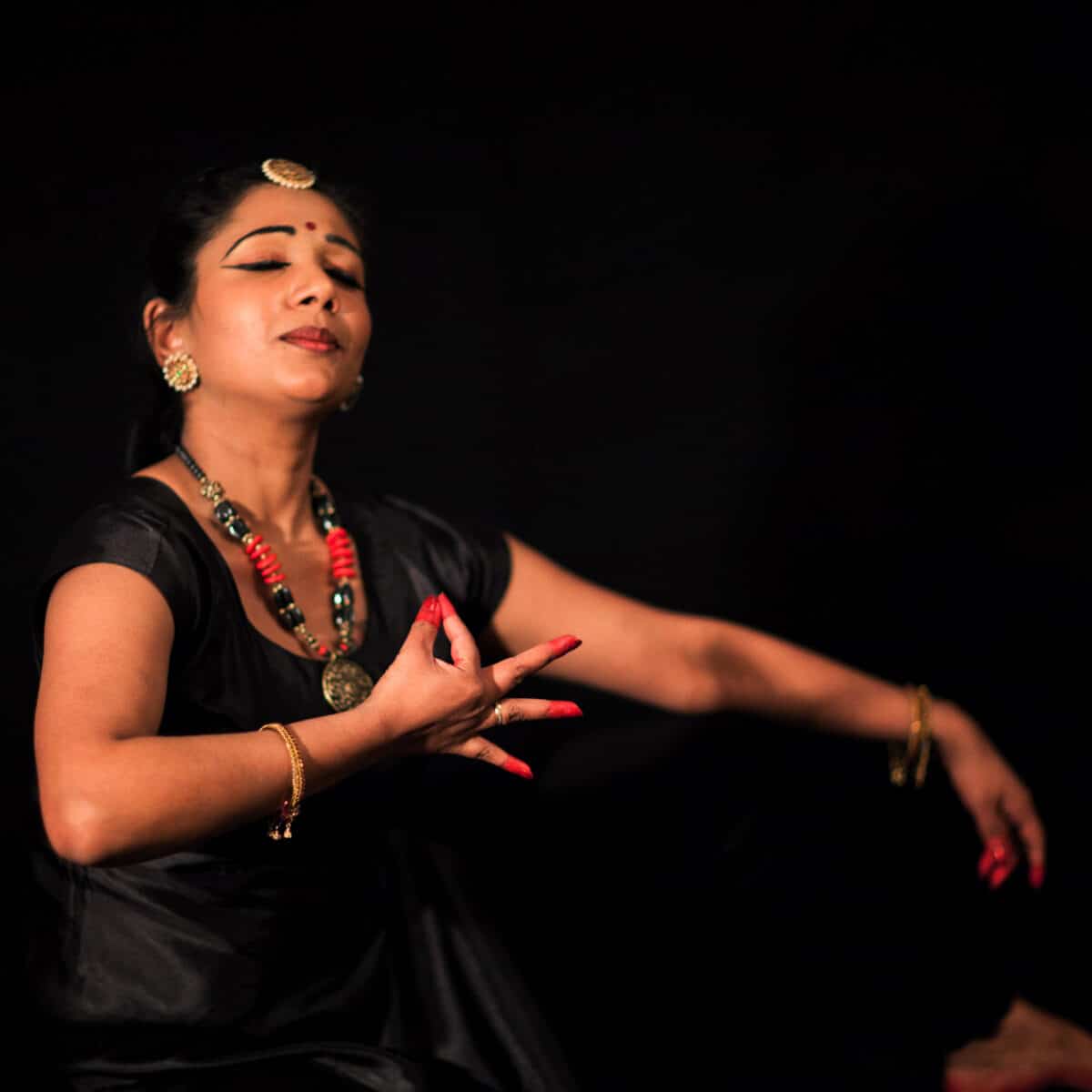 Melaninrik kvinne i sorte klær danser tradisjonsrik tamilsk dans med øynene lukket. Fotografi.