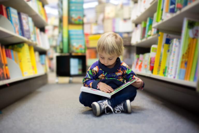 Barn som sitter på gulvet mellom bokreoler og leser i en bok
