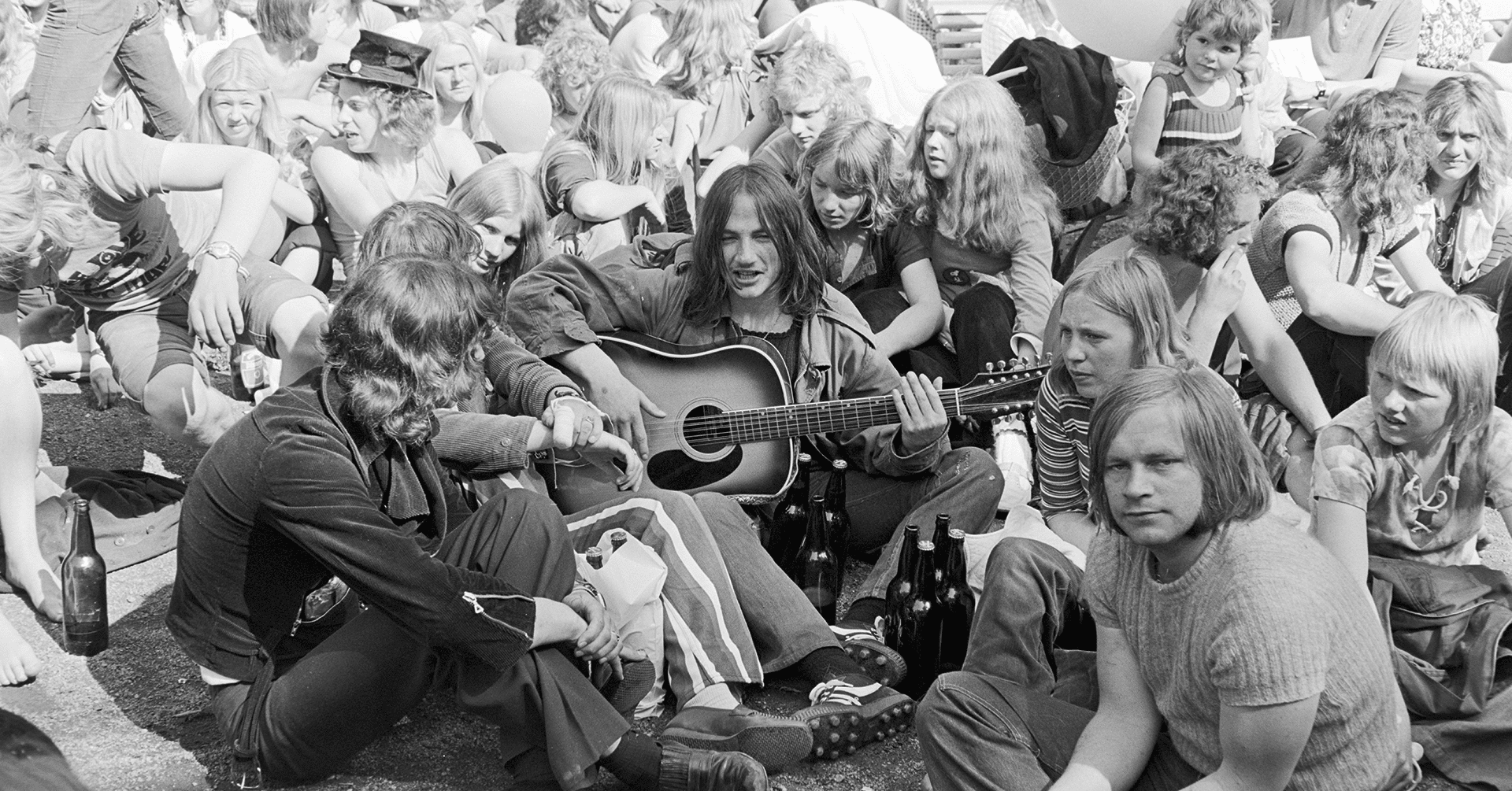 Unge menn og kvinner sitter tett sammen og spiller gitar og synger