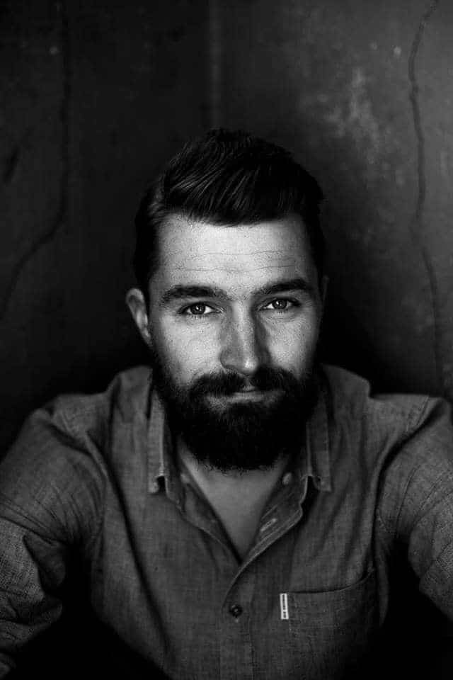 Fotografi. Sort-hvitt-bilde av en mann med mørkt hår, bart og skjegg.