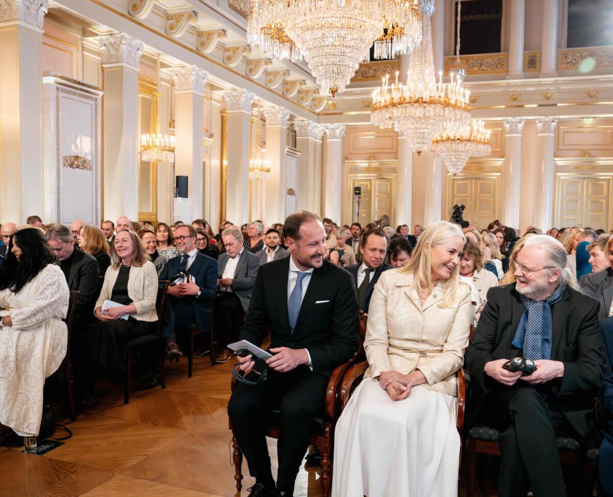 En stor forsamling mennesker er samlet i en pyntet festsal.