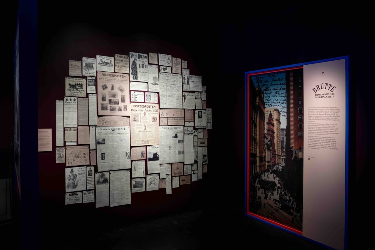 Fotografi av utstillingsrom på Nasjonalbiblioteket. En vegg fylt med gamle aviser og rekameplakater fra 1825 til 1930. Til høyre et bilde av New York med tittelen Brutte drømmers boulevard.
