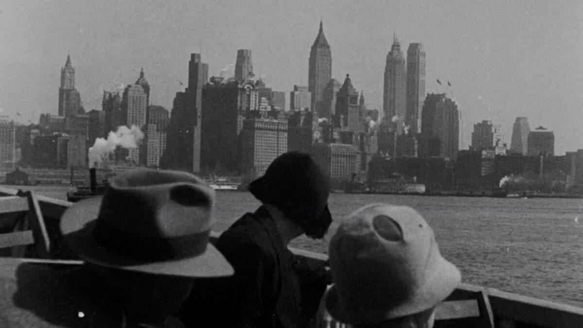 Svart-hvitt fotografi av mennesker på båt med New Yorks skyskrapere i bakgrunnen.