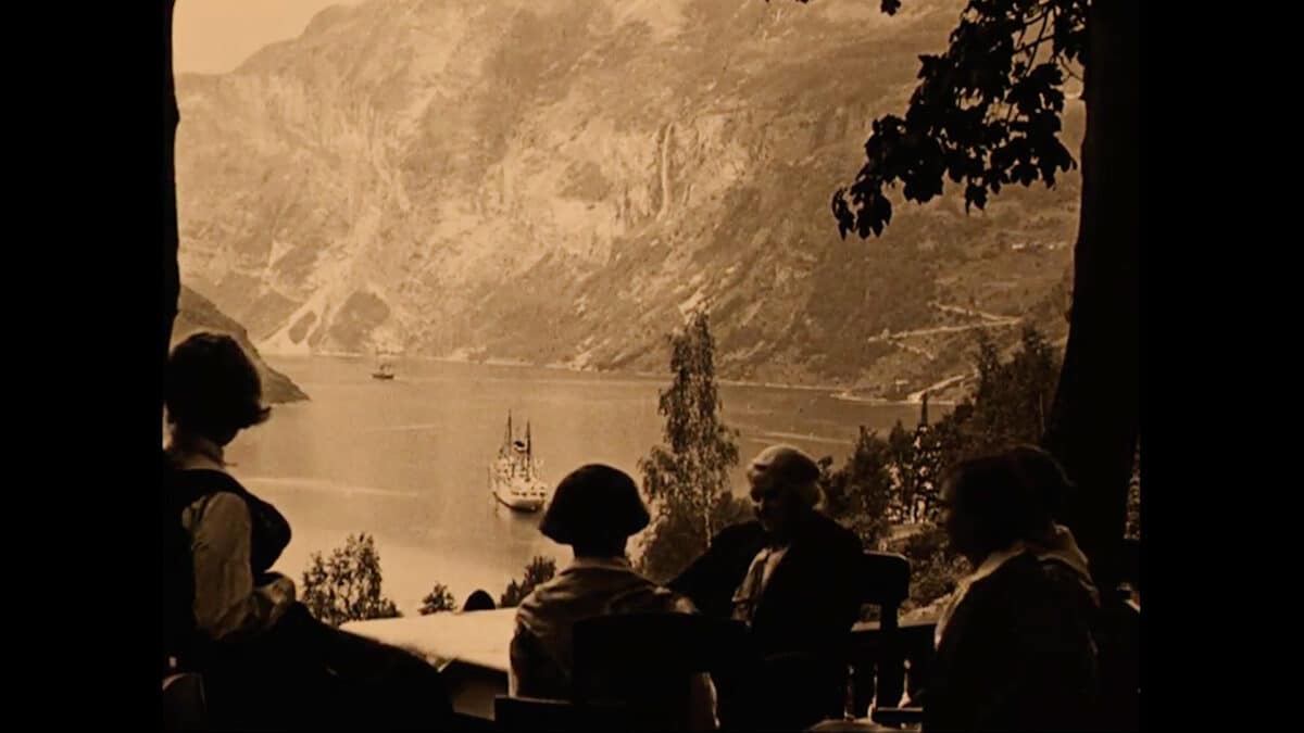 Hundre år gammelt bilde viser siluetter av mennesker som sitter og ser ned på båter i Geirangerfjorden