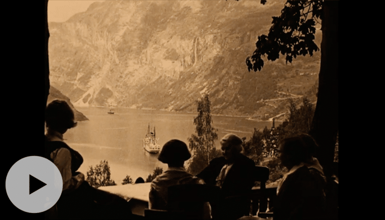 Hundre år gammelt bilde viser siluetter av mennesker som sitter og ser ned på båter i Geirangerfjorden