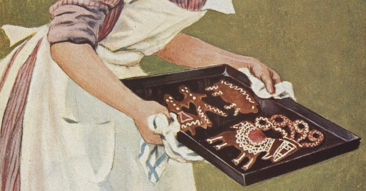 Person med forkle holder en bakeplate med pyntede pepperkakefigurer formet som dyr og andre motiver, dekorert med hvit glasur.