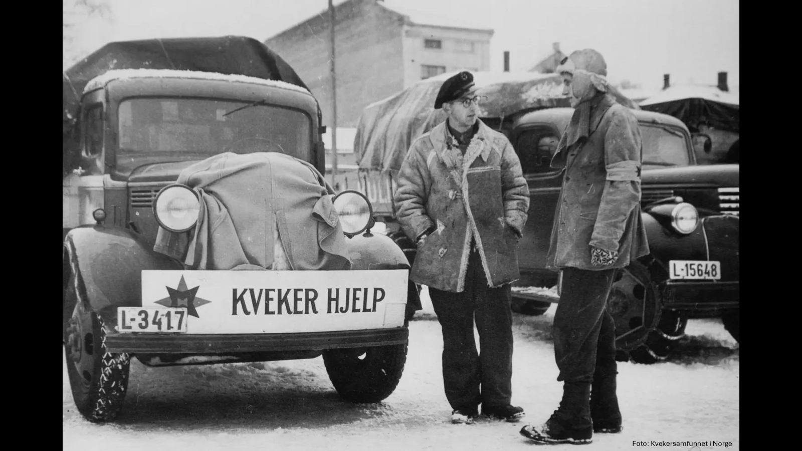 To menn snakker sammen ved siden av en gammel bil med et skilt det står "kveker hjelp" på