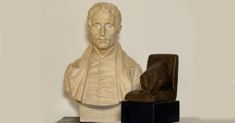 Hvit byste av en mann med lukkede øyne ved siden av årets pris som viser en hånd og utstrakt pekefinger som leser punktskrift