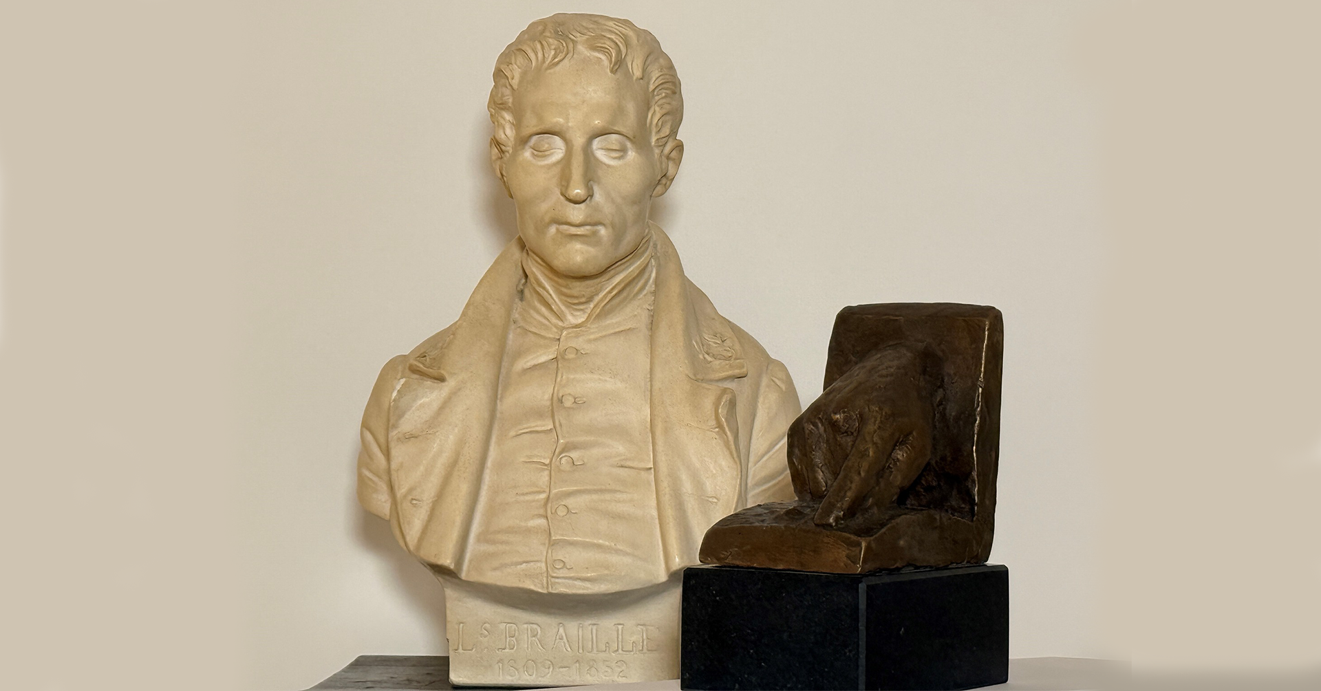 Hvit byste av en mann med lukkede øyne ved siden av årets pris som viser en hånd og utstrakt pekefinger som leser punktskrift