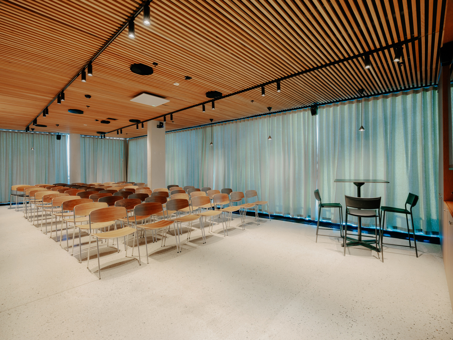 Konferanserom med tettstående rader av trestoler vendt mot en skjerm.