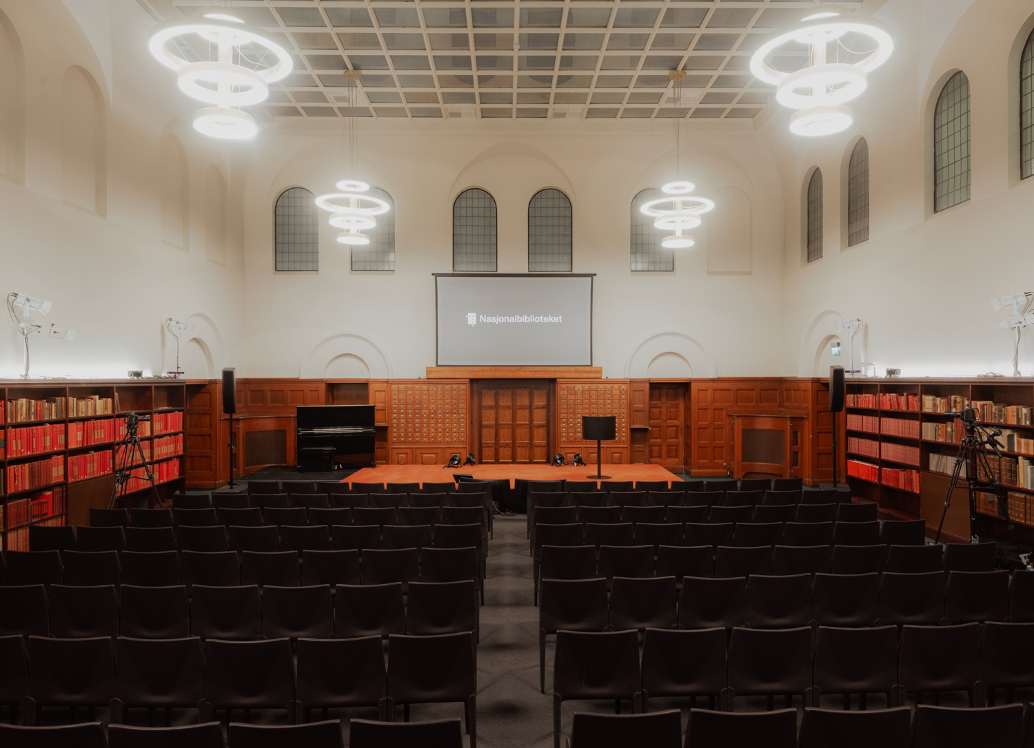 Et auditorium sett fra bakerst i rommet, med mange stoler vendt mot en scene og en prosjektorskjerm med teksten «Nasjonalbiblioteket».