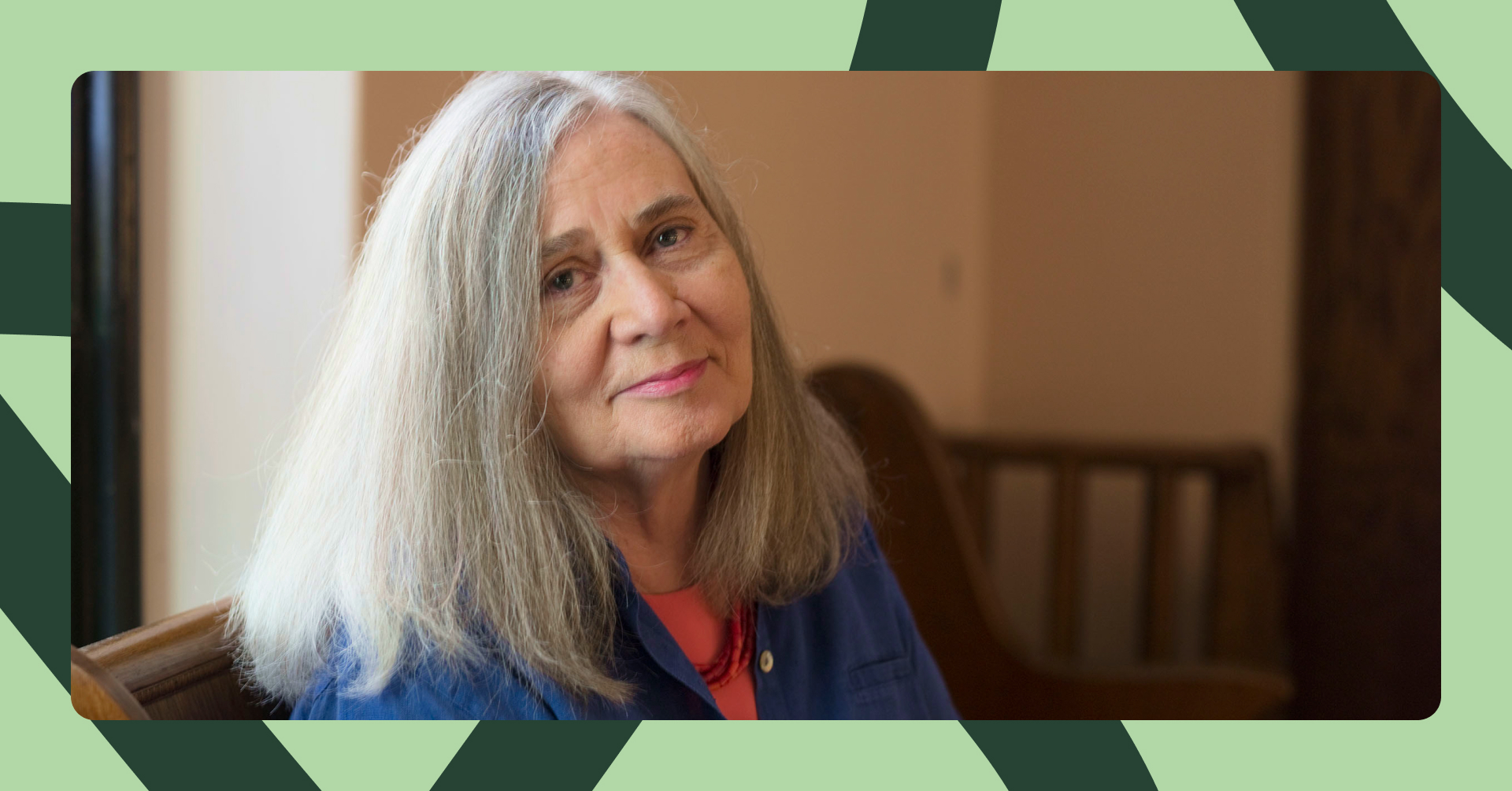 En kvinne med skulderlangt grått hår smiler mot kameraet. Hun sitter foran et vindu