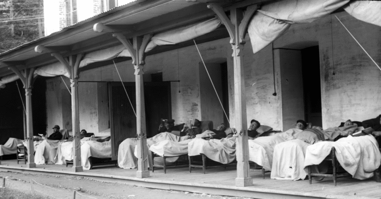 Mannlige pasienter ligger på rekke og rad på liggestoler utendørs ved et sanatorium. Noen smiler og andre leser bøker.