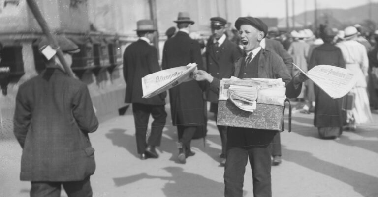 En ung gutt står med en bunke aviser og roper ut i en travel gate