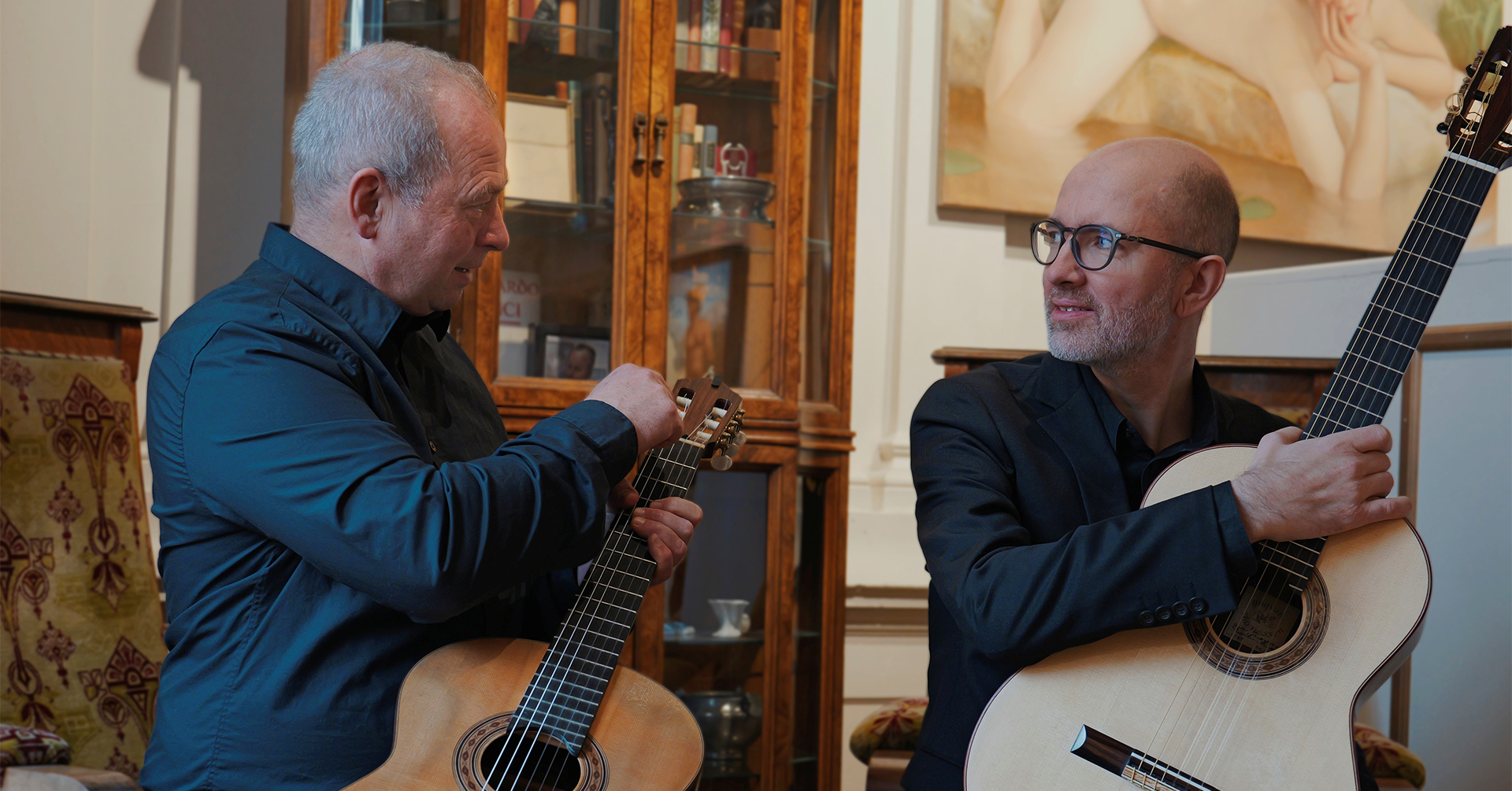 To menn sitter på en stol med hver sin gitar og snakker med hverandre