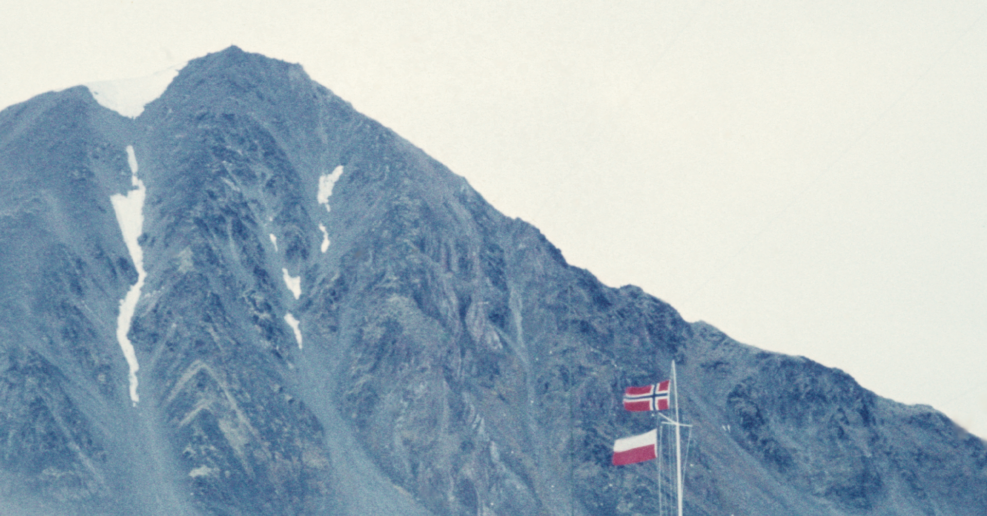 To flagg vaier i vinden, i bakgrunnen ruver et høyt fjell