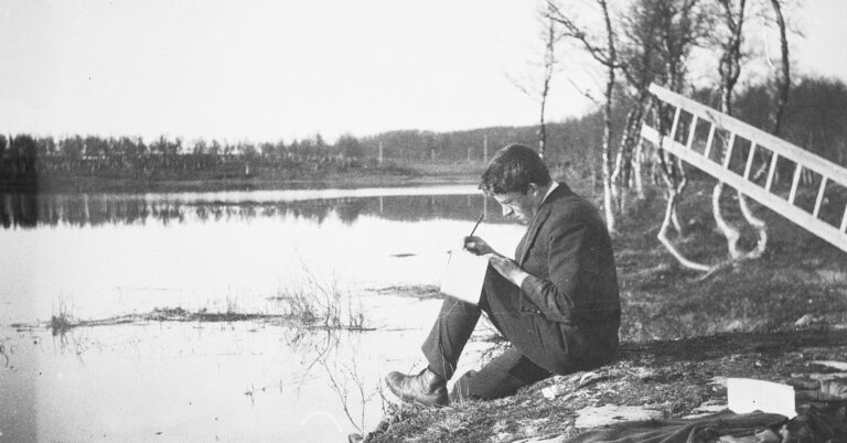Mann sitter på et berg ved et vann og skriver.