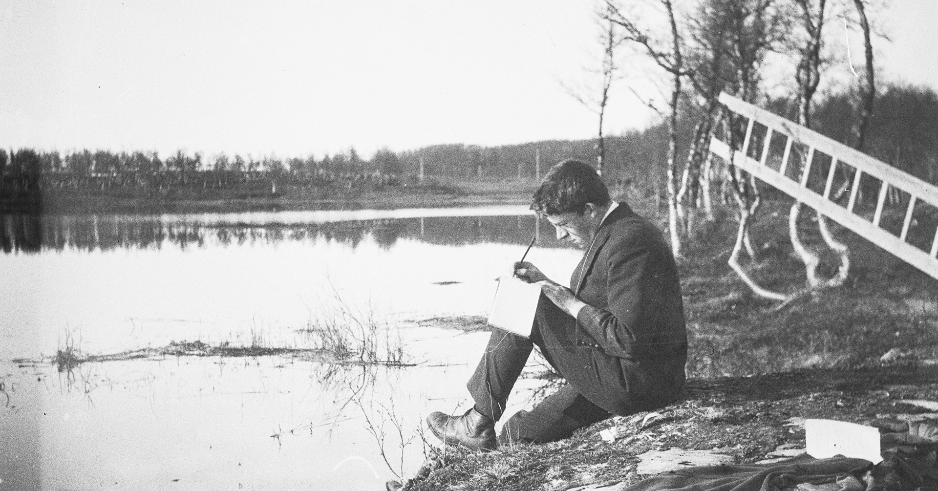 Mann sitter på et berg ved et vann og skriver.
