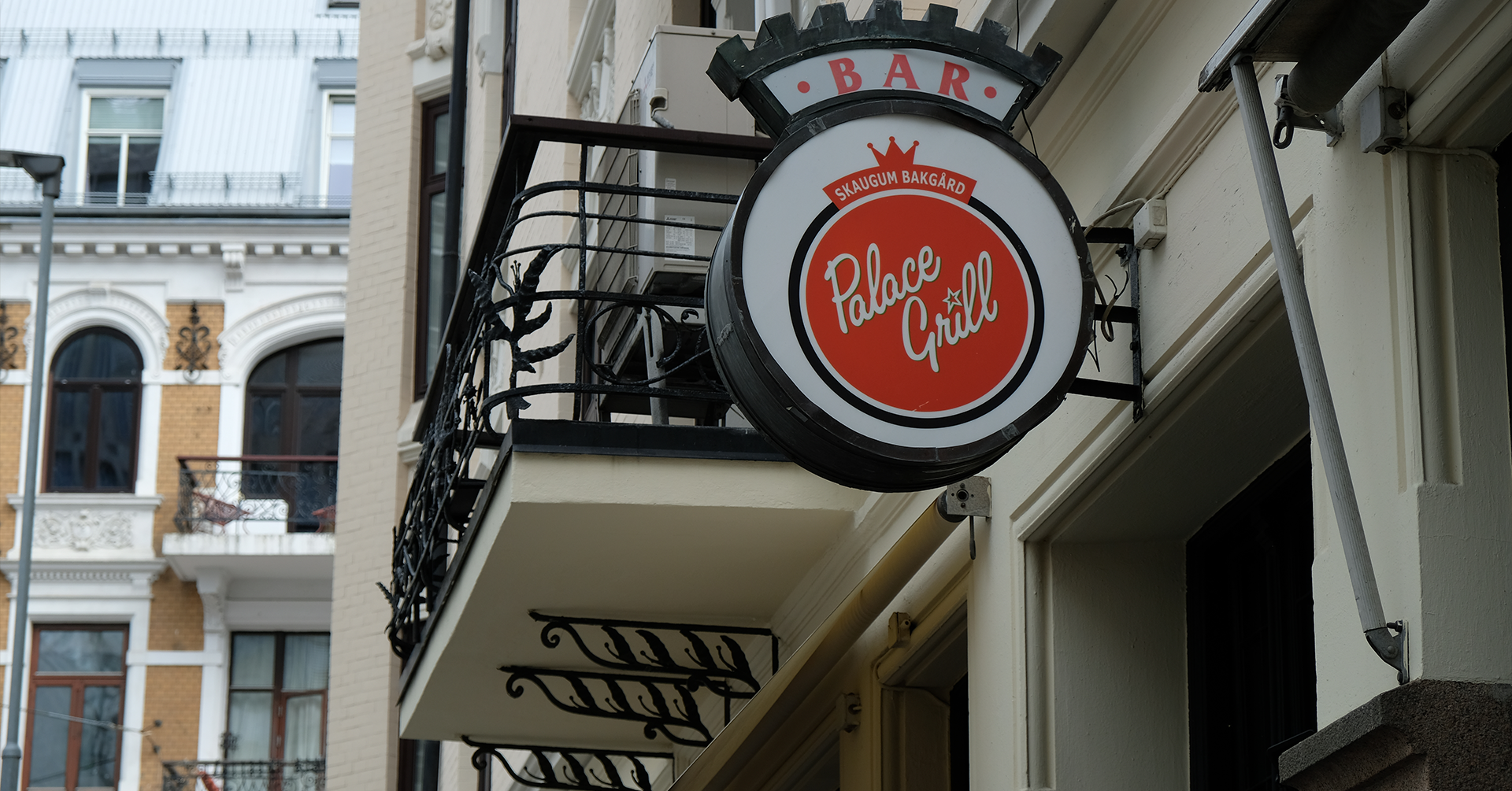 Et rundt skilt som viser logoen til en restaurant. I bakgrunnen er det en liten balkong.