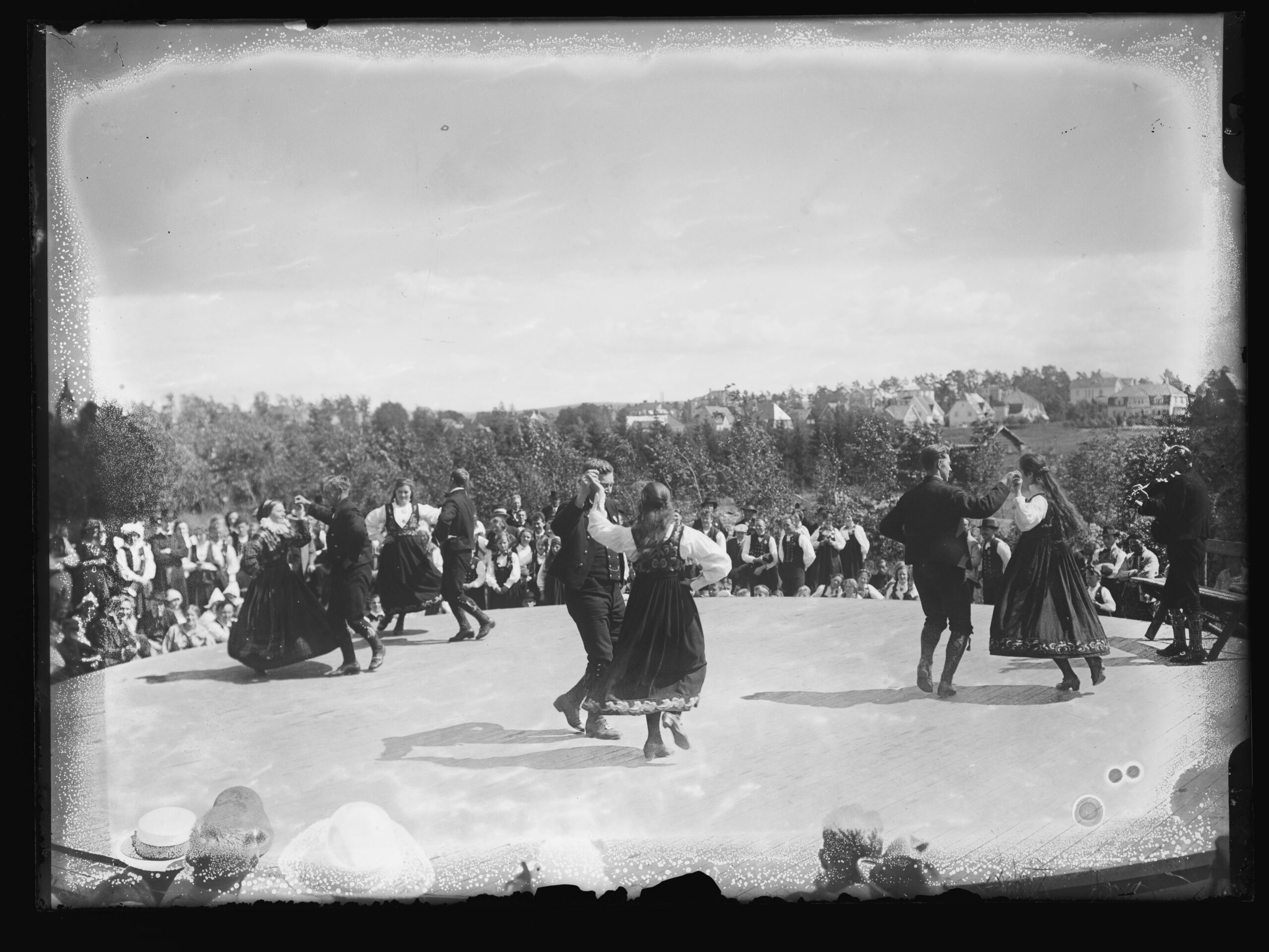 Gammelt svart-hvitt foto av folk som danser utendørs mens en stor folkemengde ser på.